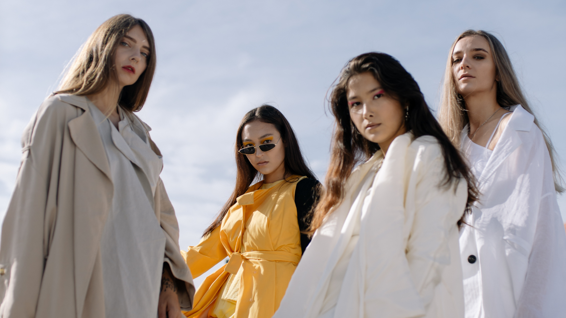 Group of four models in modern outerwear posing outdoors, showcasing contemporary fashion design.